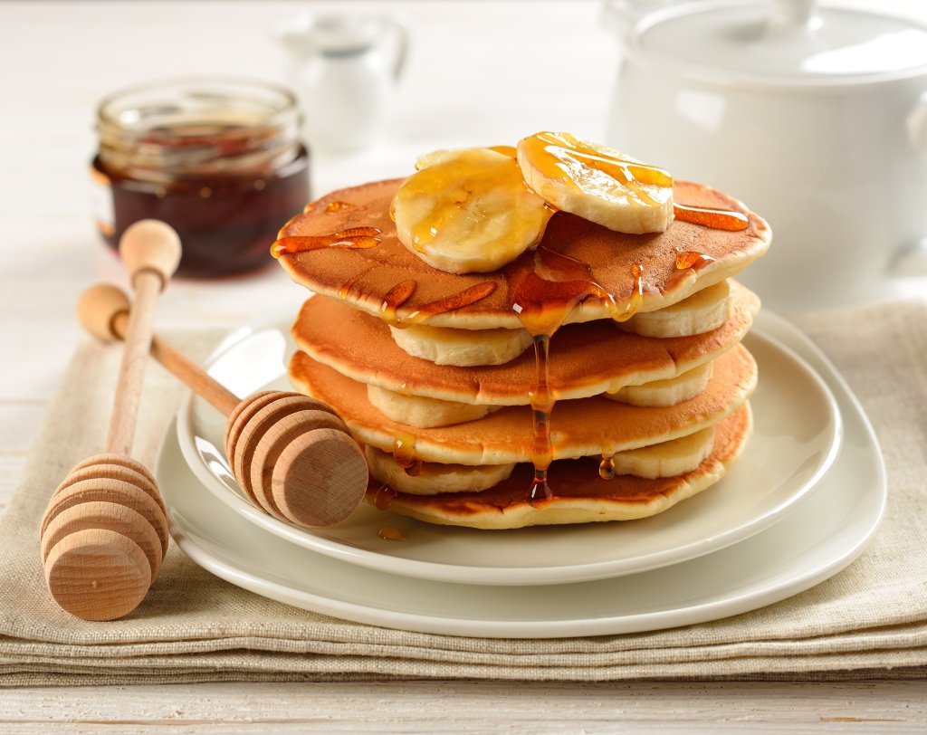 Uma pilha de panquecas servida com banana e mel.