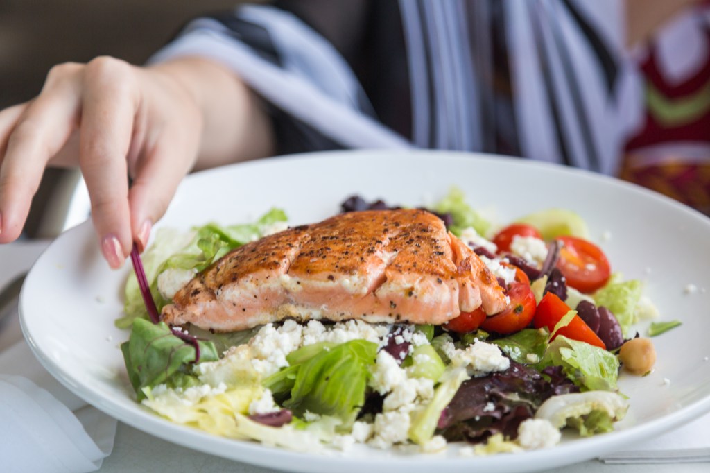 Mulher comendo prato de salada com salmão 6 alimentos que você deve comer se quer ter mais energia durante o dia