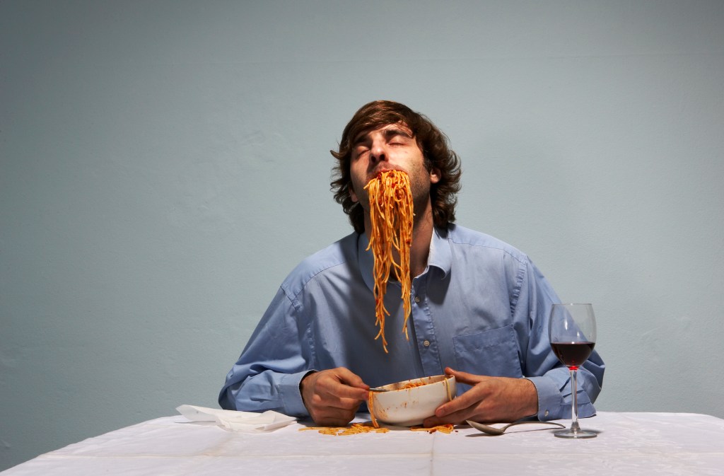 Man sitting at table, with spaghetti stuffed into mouth Nutricionista do Centro Ravenna dá 6 dicas para uma dieta de sucesso